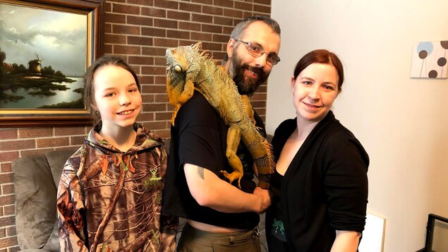 un homme, une femme et une jeune-fille entourent un reptile exotique.