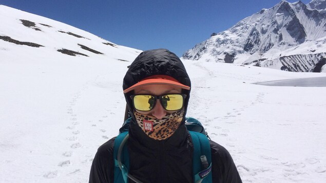 L'athlète au soleil, sur un sommet enneigé porte des lunettes et un masque de haute montage. 