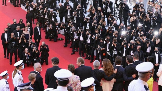 Sur un tapis rouge, des photographes pointent leurs appareils sur des acteurs.