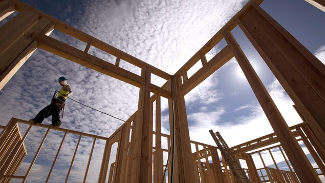 Un travailleur debout sur la structure d'une maison en construction.
