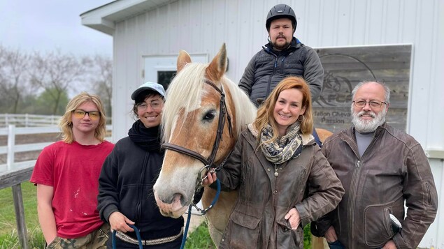 Une photo de groupe. Diane Plante et ses deux filles sont avec Raphaël, qui monte un cheval. Son père est à ses côtés et le groupe pose devant l'écurie.