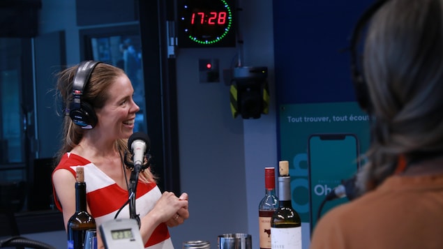 Une femme avec une robe lignée sourit en regardant à sa gauche dans un studio de radio.