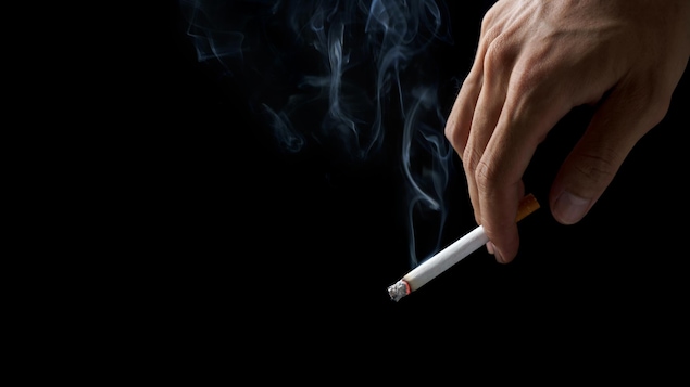 Plan serré sur une main qui tient une cigarette allumée.