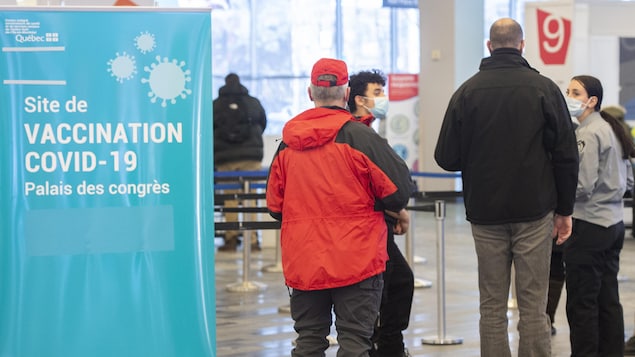 Des gens attendent en ligne pour recevoir une dose de vaccin contre la COVID-19 au site de vaccination du Palais des congrès de Montréal. 