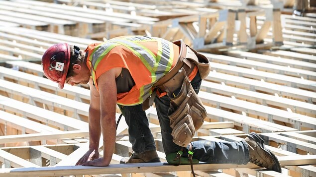 Un travailleur en construction est accroupi sur des planches de bois qui formeront un toit ou un plancher d'une bâtisse.