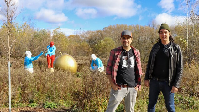 Deux hommes dans un parc avec en arrière-plan une œuvre représentant personnages autour d'une pomme géante.