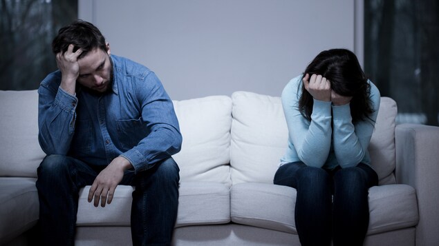 Vue sur un sofa, où l'on voit un homme et une femme en position recroquevillée, la tête dans les mains.