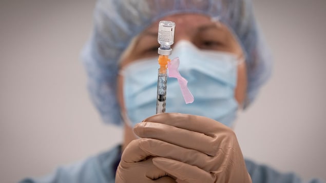 A nurse holds a syringe in her hands and extracts liquid from a small vial.
