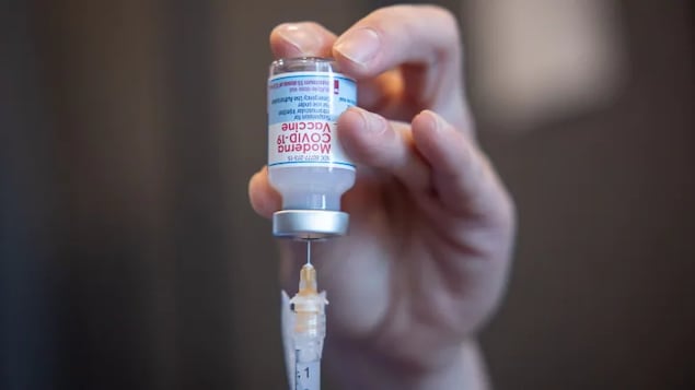 Très gros plan d'une seringue et de la bouteille contenant le vaccin, tenues dans une main.