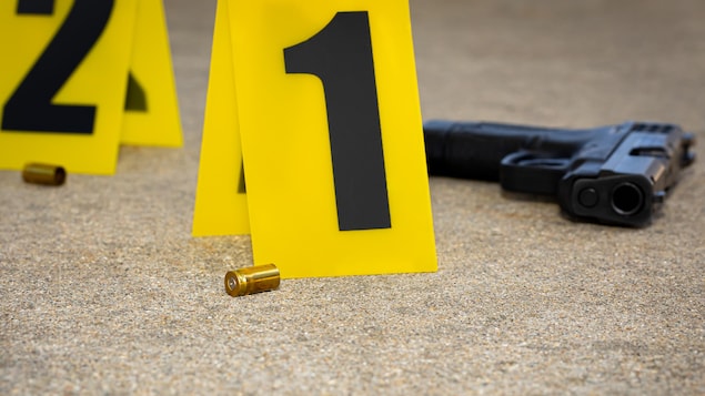 Une arme et deux douilles sont sur le sol, sur une scène de crime.