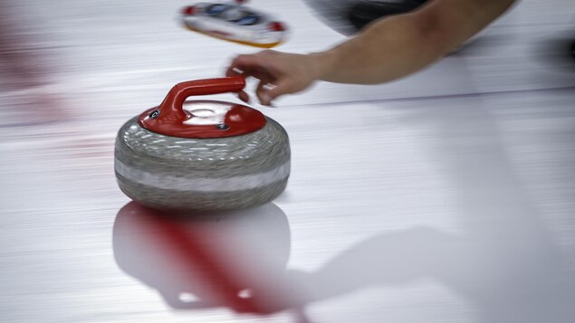 Une pierre de curling est lancée sur la glace.