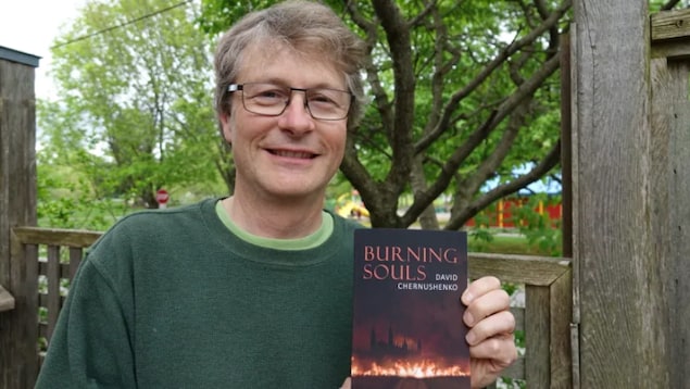L'auteur, à l'extérieur, montre la couverture de son livre. 