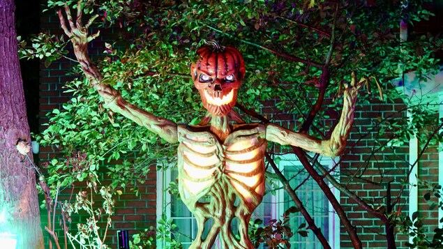 une décoration d'Halloween. Un squelette avec une tête de citrouille devant une maison résidentielle. 
