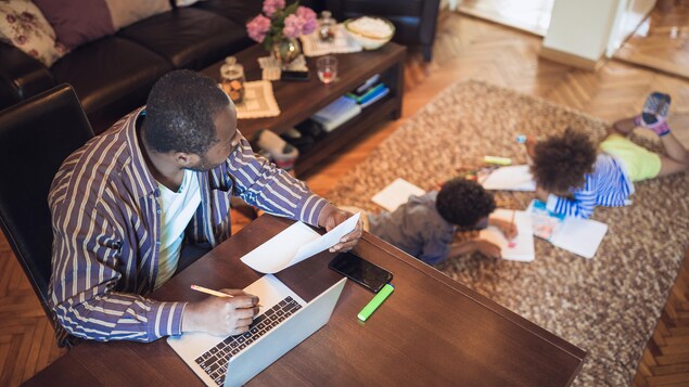 Un père de famille effectue du télétravail pendant que des enfants font des devoirs