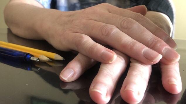 Deux mains croisées sur une table des crayon à mine à la gauche