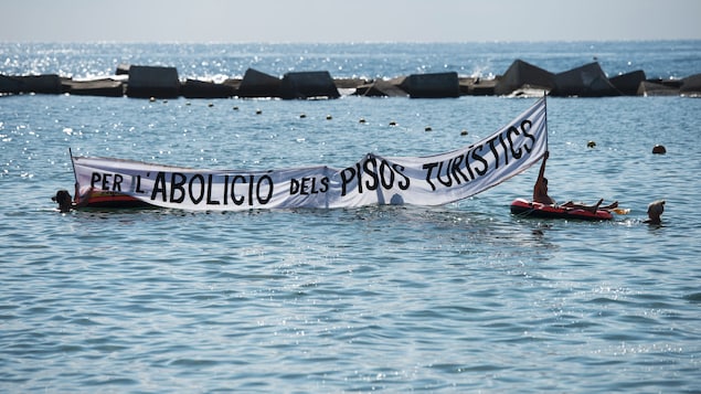 Des résidents déroulent une bannière face à la plage où il est écrit «Pour l'abolition d'appartements touristiques ».