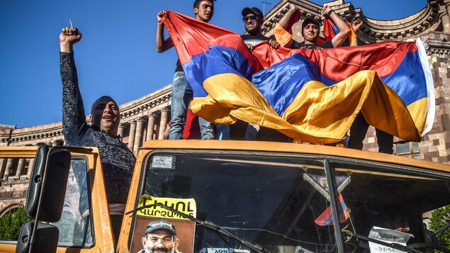 Des manifestants arméniens tenant le drapeau de l'Arménie debout sur la toiture d'une camionnette sur la quelle se trouve une affiche du chef de l’opposition Nikol Pachinian.