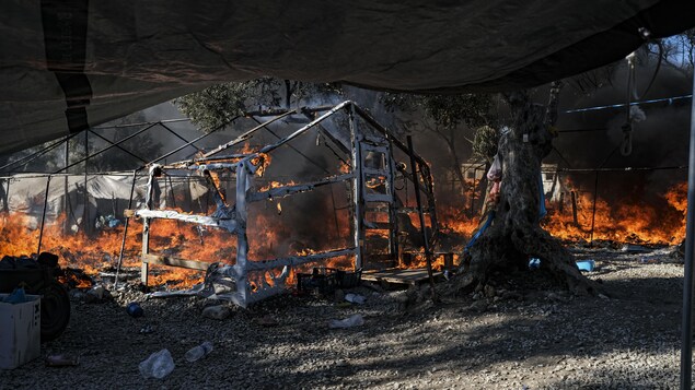 Les ruines du camp de réfugiés encore en proie aux flammes. Il ne reste que les piquets des tentes qui tiennent encore debout. 
