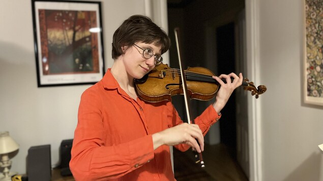 Une jeune femme avec une chemise orangée joue du violon.