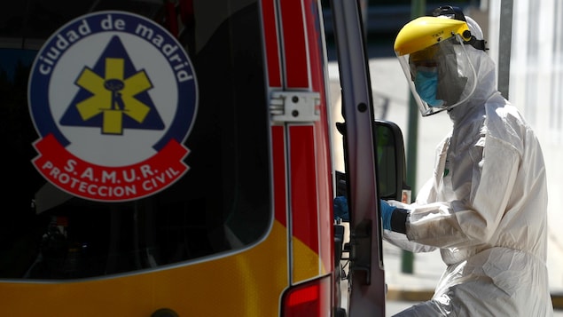 Un paramédic porte son équipement de protection devant une ambulance. 