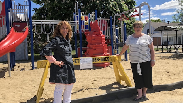 Deux femmes posent devant un module de jeux pour enfants dans un parc.
