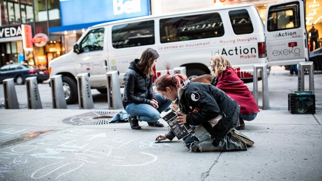 Des jeunes dessinent avec une craie des dessins à même le sol sur la rue Sainte-Catherine à Montréal