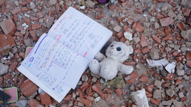 Un jouet et un carnet de notes gisent parmi les débris près d’un immeuble à logement.