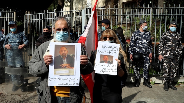 Deux personnes masquées portent des pancartes avec la photo de Lokman Slim.