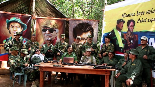 Des personnes armées assis autour d'une table dans une forêt avec des affiches de personnages de révolutionnaires à l'arrière.
