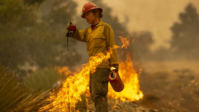 Une pompière se sert d'une torche pour combattre un feu.