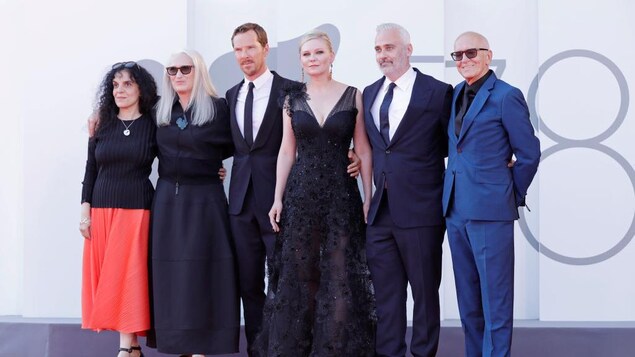 Trois femmes et trois hommes posent sur un tapis rouge. 