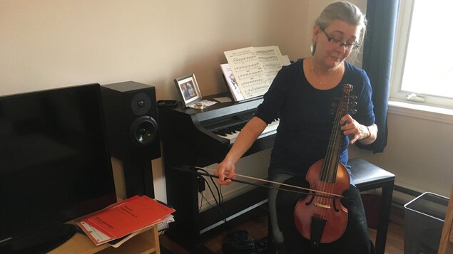 Une musicienne dans la soixantaine joue de son violon dans une pièce de son appartement.