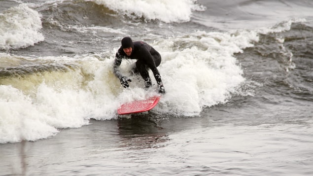 Un surfer vêtu d'une combinaison complète prenant une vague.