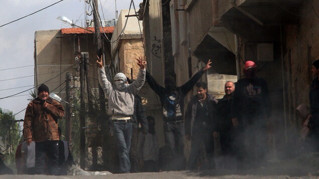 Des manifestants dans les rues de Deraa. Deux d'entre eux sont masqués et font le V de la victoire.