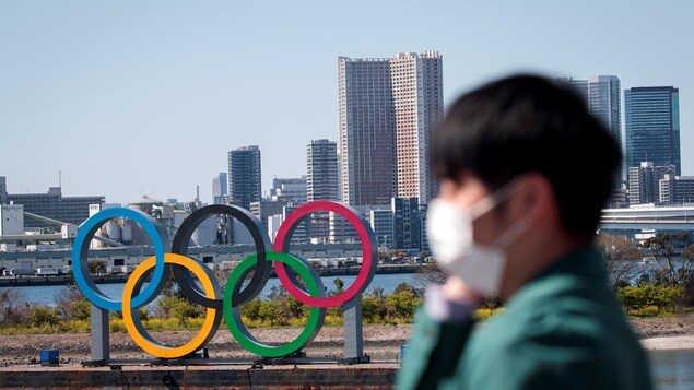 Un homme portant un masque marche devant les anneaux olympiques à Tokyo.