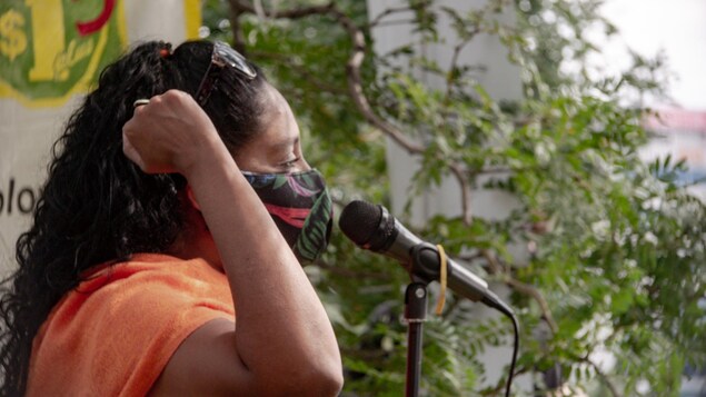 Une femme portant le masque avec le bras dans les airs devant un micro.