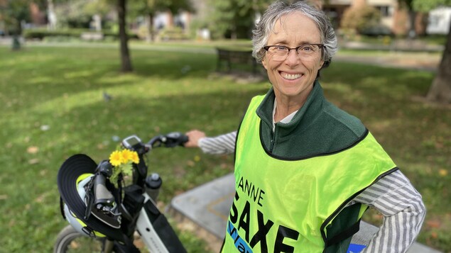 Dans un parc, Diane Saxe habillée en gilet vert tient un vélo