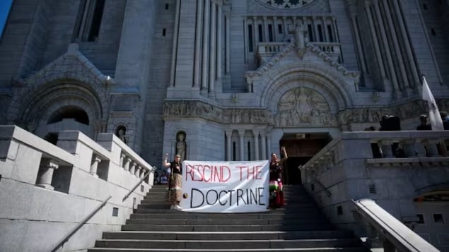 Sarain Fox, right, and Chelsea Brunelle of the Batchewana First Nation unfurled a banner reading 'Rescind the Doctrine' outside the mass presided over by Pope Francis at the National Shrine of Saint Anne de Beaupre in Quebec last summer. (John Locher/The Associated Press)