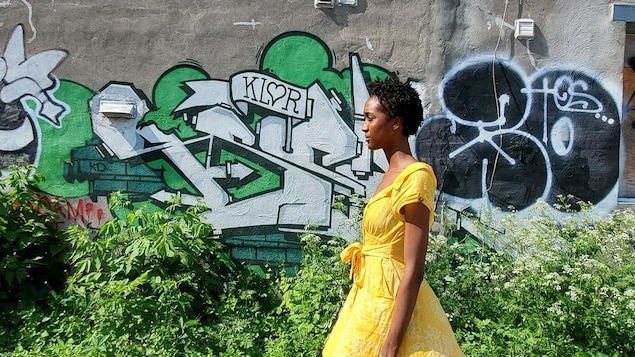 Une femme habillée d'une robe jaune, marche devant un mur couvert de graffitis.