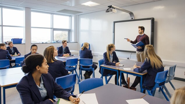 Un jeune enseignant donne cours à une classe d'adolescents en uniformes scolaires bleus.