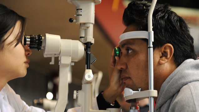 Une optométriste réalise un examen de la vue sur un homme dont le menton et le front sont appuyés contre un instrument pour stabiliser son visage.