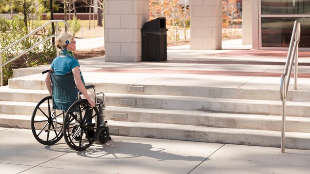 Une femme en fauteuil roulant s'arrête devant un escalier.