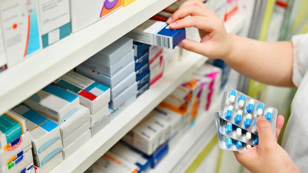 Une pharmacienne tient des médicaments dans ses mains, derrière le comptoir.