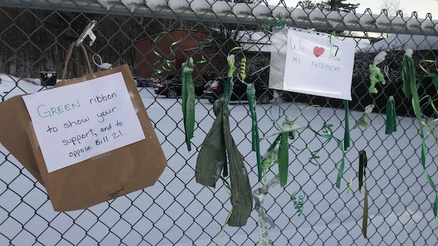 A hand-drawn poster in support of teacher Fatemeh Anvari is surrounded by green ribbons on a chain-link fence outside Chelsea Elementary School in Chelsea, Que. Recently, the school principal told the Grade 3 teacher she had to move to a position outside the classroom because she wears a hijab. Under Quebec's Bill 21, some civil servants — including teachers — can't wear religious symbols at work. 