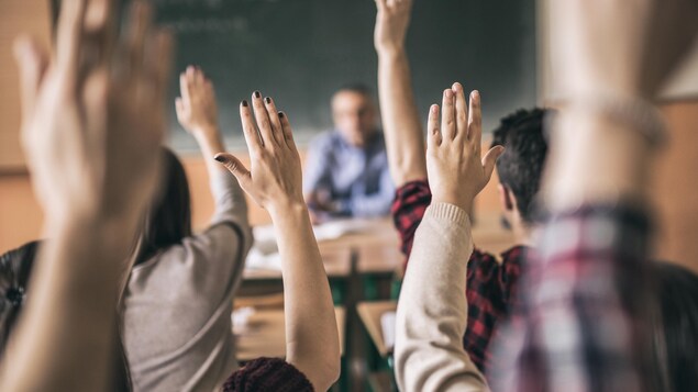 Des mains levées dans une classe.