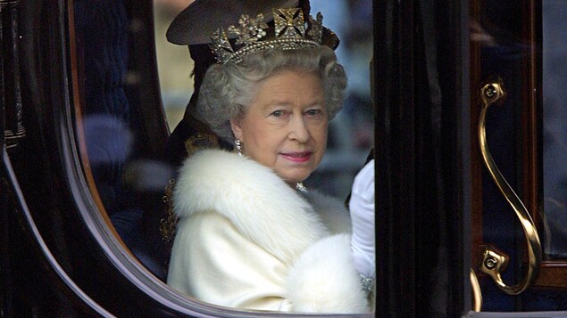 Photo de la souveraine portant sa couronne prise à travers la fenêtre du carrosse royal.