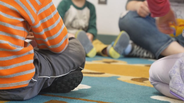 Des enfants assis en cercle par terre sur un tapis, dans une classe.