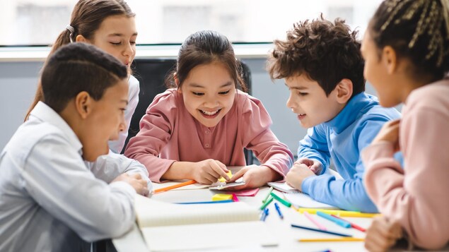 Des enfants assis autour d'une même table s'amusent avec une calculatrice, du papier et des crayons. 