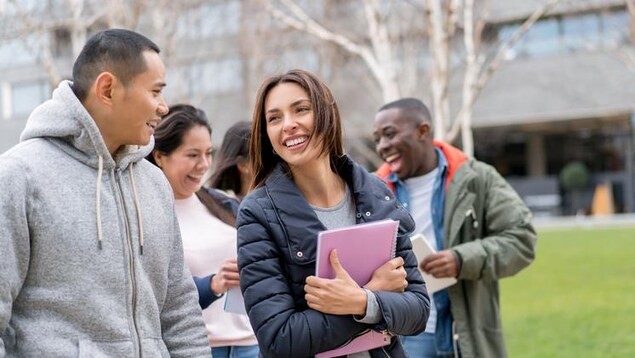 Cinq étudiants étrangers discutent en marchant sur un campus universitaire. 