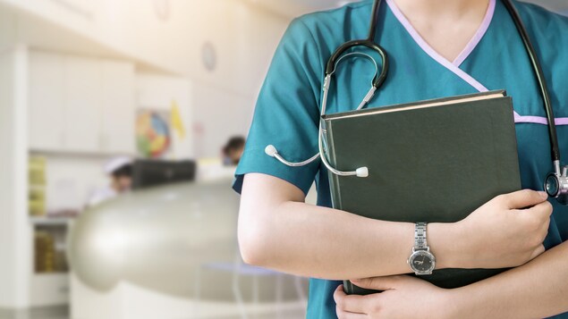 Une infirmière, stéthoscope au cou et livre en main.